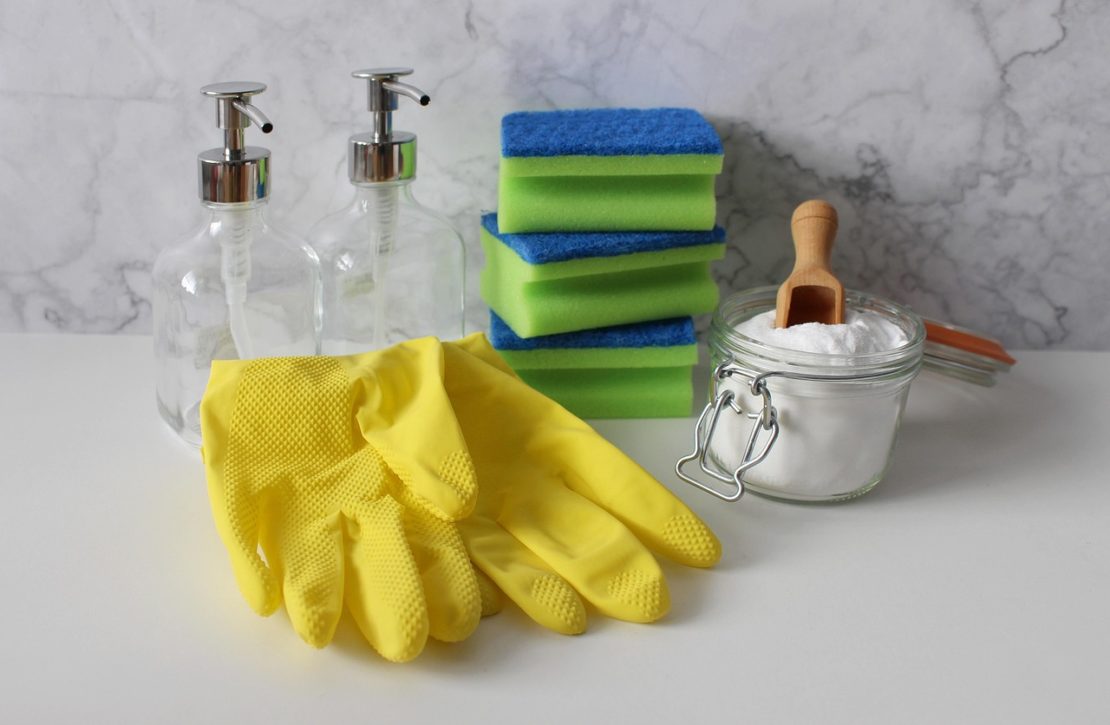 Yellow gloves, glass soap dispensers, sponges, and a jar of baking soda on a white surface.